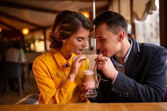 Young couple sharing a layered coffee drink in a cafe