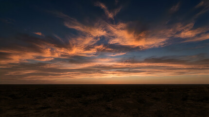 Obraz premium Vibrant orange sunset sky over a dark desert horizon landscape during the golden hour of the late evening