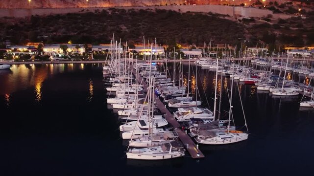 Night harbor view with colorful lights and moored vessels filmed by drone in Kas. Illuminated walkways and marina signs. Festive yet relaxed evening energy perfect for nightlife and travel marketing
