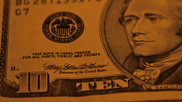 Macro ten dollar banknote featuring Hamilton portrait and Federal Reserve seal in warm golden light