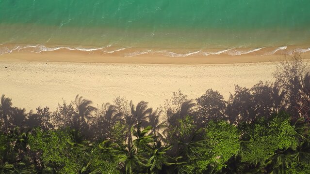 Aerial view of a pristine sandy beach with turquoise water and palm trees casting long shadows on the sand in Thailand, Thailand.