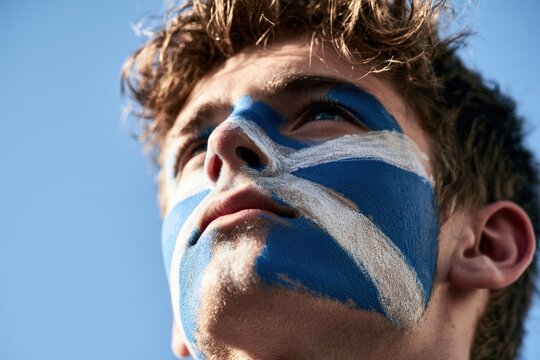 Blue and white face paint on young male soccer fan gazing upward against clear blue sky