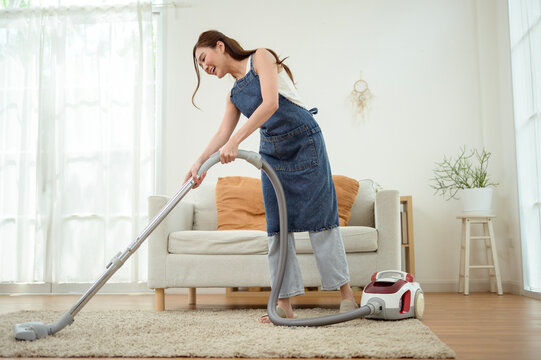 Asian Woman Vacuuming Carpet While Cleaning Bright Modern Home