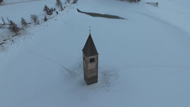 Aerial view of the historic Curon Bell Tower rising from the frozen surface of Lake Reschen in Graun im Vinschgau, Trentino-Alto Adige, Italy.
