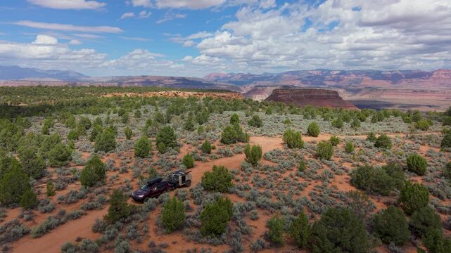 Aerial view of SUV towing a teardrop camper trailer overland across Gooseberry Mesa with Zion National Park in the distance under a cloudy sky.