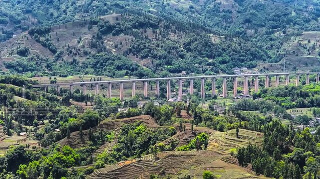 High angle shot of a long highway bridge spanning lush green mountain valleys and terraced tea plantations in Ya'an, Sichuan.