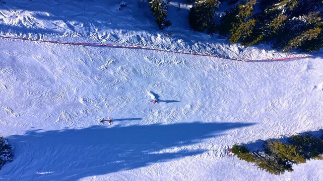 Aerial view of a snowy high-altitude ski run with skiers descending. Red safety ribbons. Winter sports on a sunny day. Muntain piste, Pamporovo.