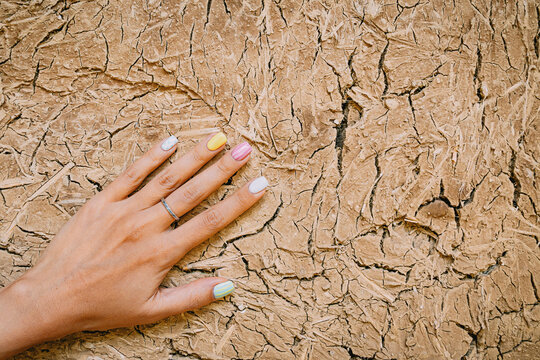 Woman's hand with colorful painted fingernails gently touching a rough, cracked mud wall surface, showing contrast between delicate and rugged