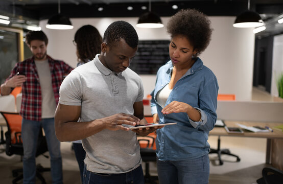 Diverse people discussing project data near colleagues in coworking