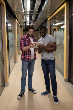 Young diverse men discussing project data in hallway in coworking
