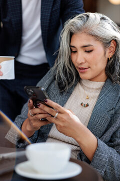 Woman with gray hair using phone, man with coffee.