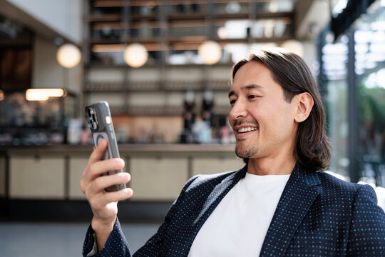 Smiling man in blazer uses phone in cafe