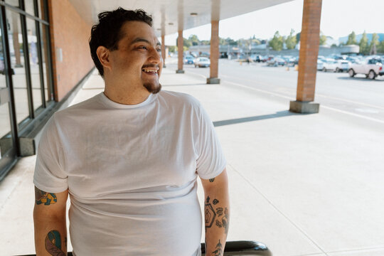 Candid man with tattoos smiling outside a suburban shopping cent