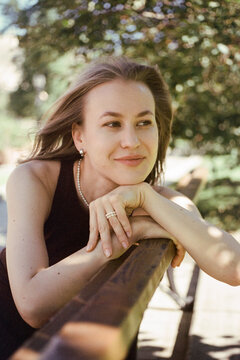 A woman leans on a wooden bench and smiles gently away