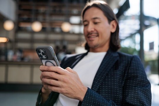 Man in blazer smiles while using smartphone indoors.
