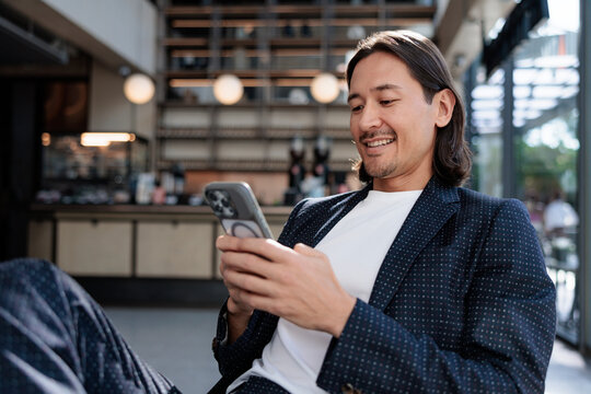 Smiling man in suit using phone in cafe.