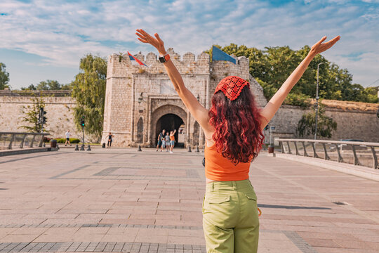 Young woman raising arms, feeling happy and free while exploring historical Nis Fortress in Serbia on a sunny summer day