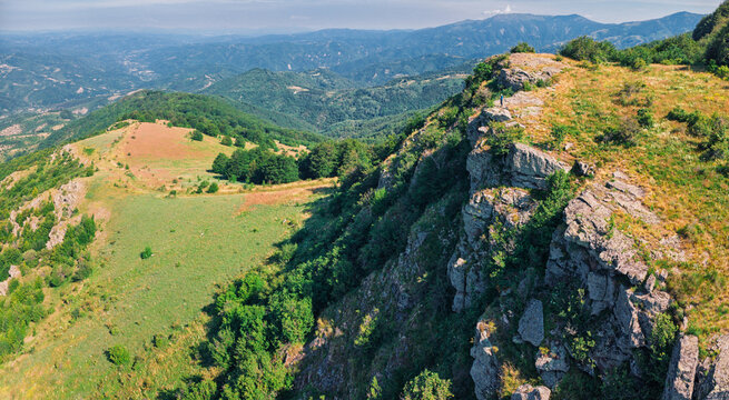 Aerial view of rocky mountain ridge with lone hiker and green valleys stretching to distant peaks. Hiking and adventure concept.