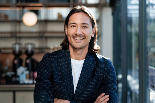 Smiling man in blazer with arms crossed indoors.
