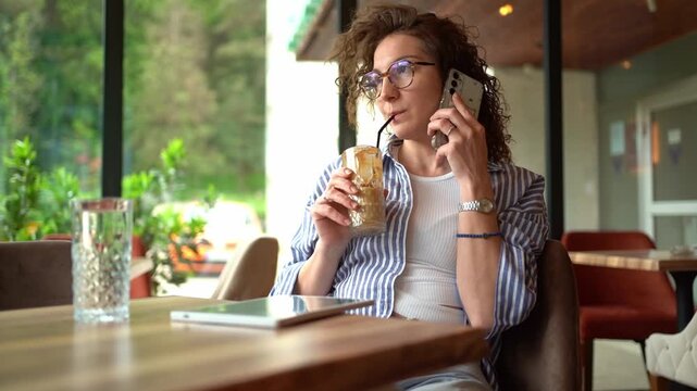 Young woman drinking iced coffee while talking on the phone