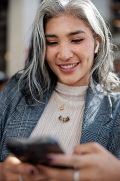 Smiling woman with silver hair uses her phone.
