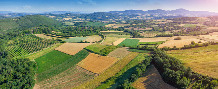 Aerial panoramic view of colorful patchwork farmland, orchards, and forested hills stretching to distant mountains. Rural landscape concept.