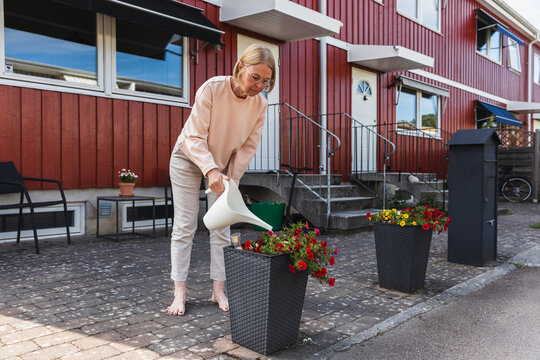 Senior woman watering colorful flowers in outdoor planter box