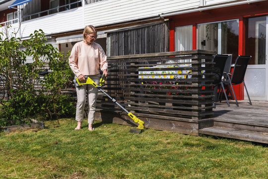 Senior woman trimming lawn edge with battery grass trimmer