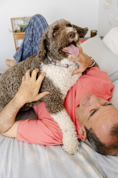 Senior man relaxing in bed with affectionate curly dog on chest