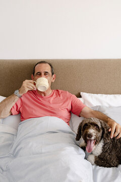 Senior man enjoying morning drink in bed with companion dog
