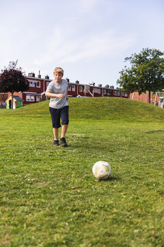 Young boy running after soccer ball on sunny grass field