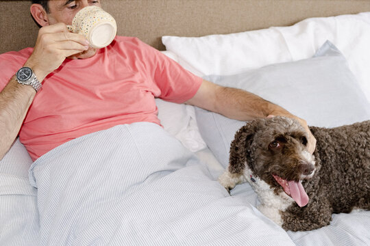 Senior man enjoying morning coffee in bed with companion dog