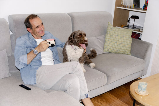 Senior man enjoying coffee at home with curly companion dog flash