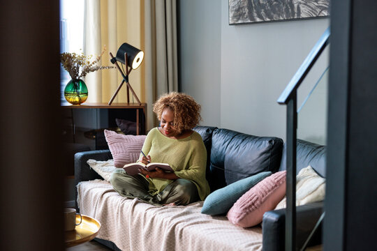 A woman writing in a journal on a cozy sofa