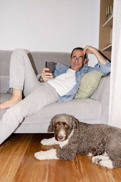 Older man browsing phone at home with dog lying in foreground