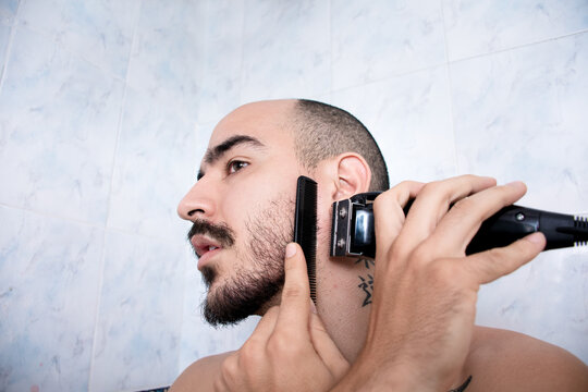 Man Shaving His Beard in a Bathroom With a Comb and Trimmer