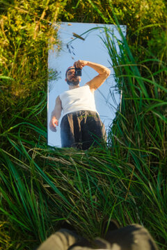 Man Takes Selfie in a Mirror Placed on Grass In Summer