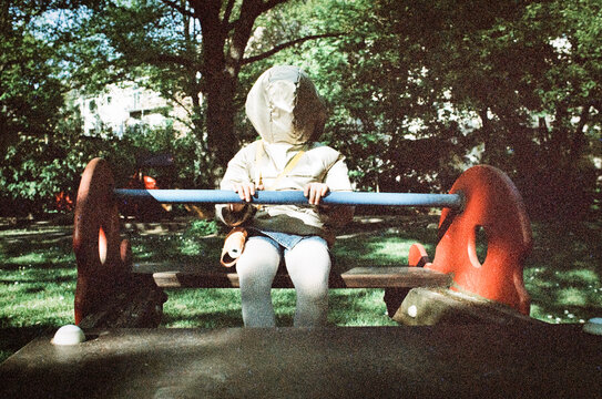 Child sitting on playground seesaw in shaded park