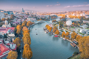 Aerial view of Tbilisi, Georgia, showcasing the Mtkvari river, Rike Park, and urban landscape during autumn © EdNurg