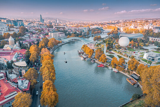 Aerial view of Tbilisi, Georgia, showcasing the Mtkvari river, Rike Park, and urban landscape during autumn