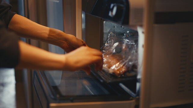 Close-up of woman's hands placing a baking tray with a roasting bag into an open portable electric oven. Preparing food for baking in a warm kitchen. Cooking meal at home.
