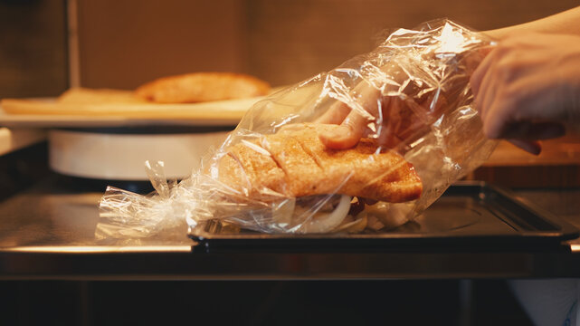 Person places raw seasoned duck breast fillets into an oven roasting bag with sliced onions on a baking sheet. Close-up of the process of preparing poultry for roasting in a home kitchen. 