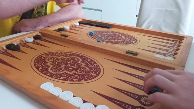 Backgammon game with hands. Wooden backgammon board. Hands moving pieces. Blue dice visible. Decorative brown pattern. Horizontal photo.