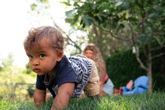 Candid toddler crawling on grass in backyard with mother nearby