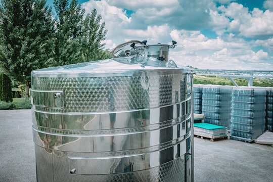 Stainless steel fermentation tank outdoors at a winery facility on a sunny day.