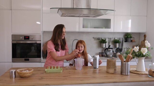 Mother and daughter breaking eggs while making Christmas cookies icing