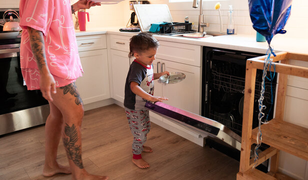 Candid family moment of a child loading dishwasher in kitchen