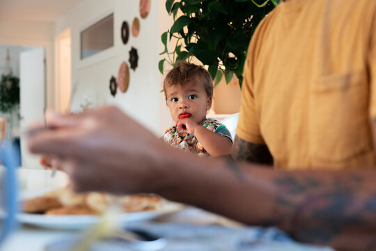 Candid toddler eating with parent at home breakfast table
