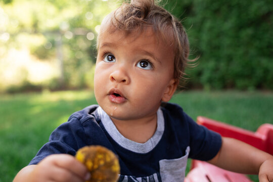 Curious toddler portrait outdoors looking up with snack and wonder