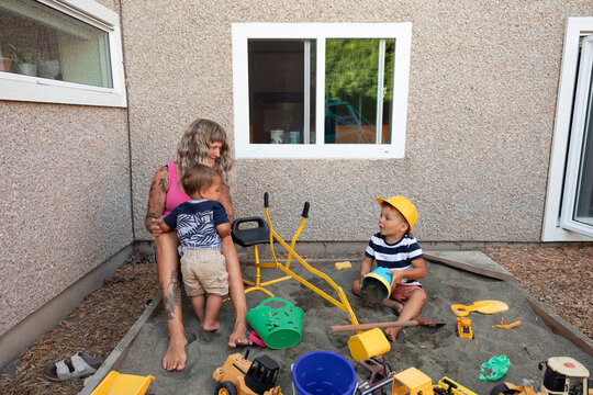 Candid mother and children playing in backyard sandbox